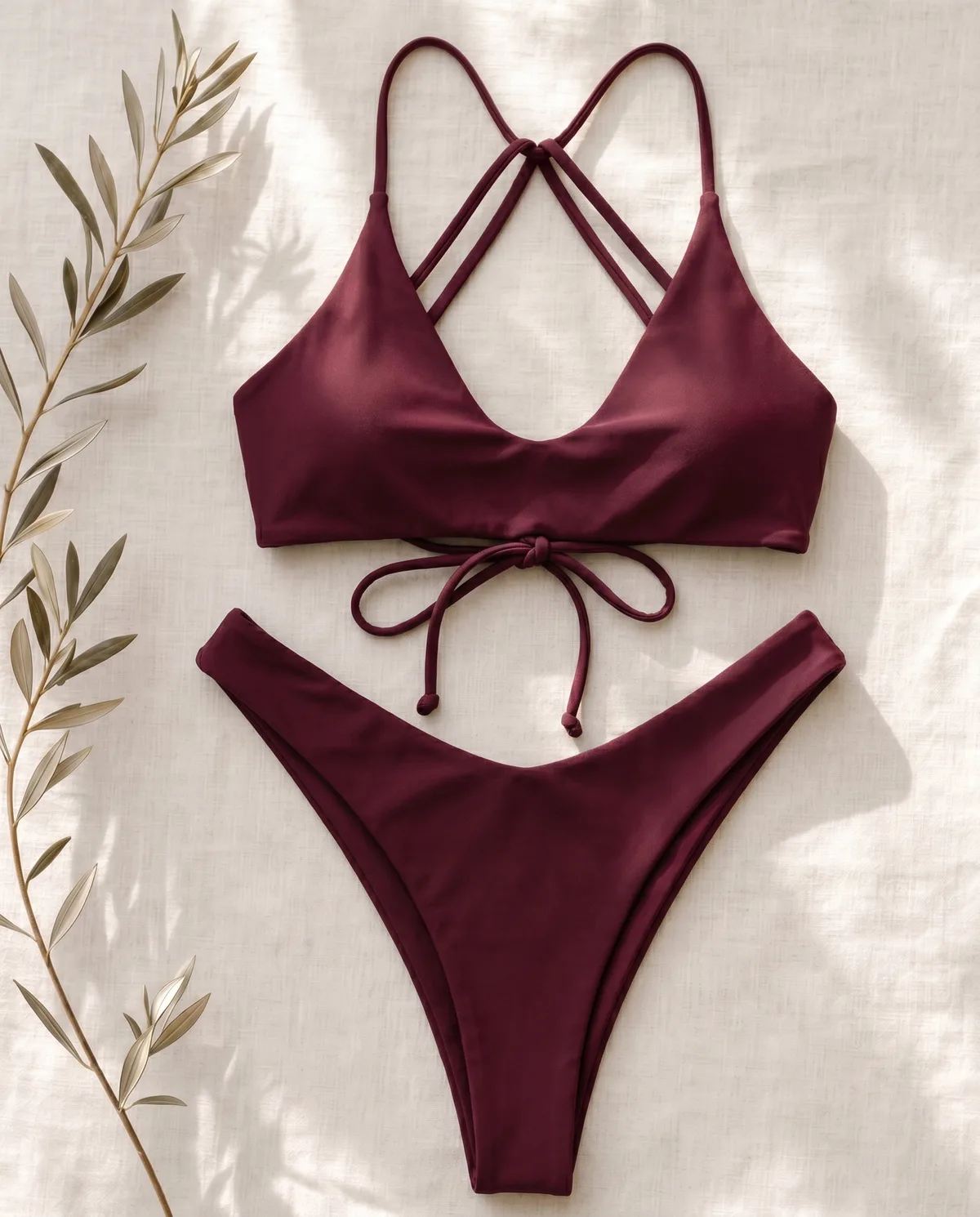 Maillot Pampelonne coloris grenat, à plat sur lin naturel avec une branche d'olivier.